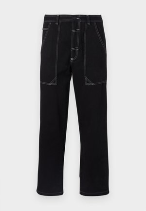 Calças pretas feitas de um tecido resistente. Apresentam costuras brancas contrastantes, múltiplos bolsos e um design de perna reta.
