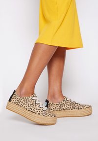 Leopard print espadrille shoes featuring a woven jute sole, beige upper, and cream laces with a black heel accent.
