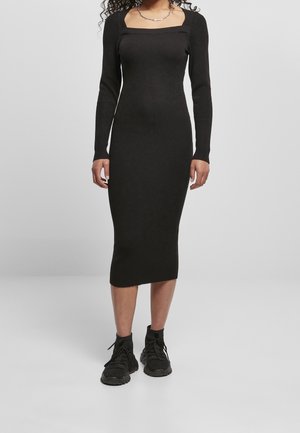 Black ribbed knit dress with a square neckline, long sleeves, and a midi length, paired with black athletic shoes.