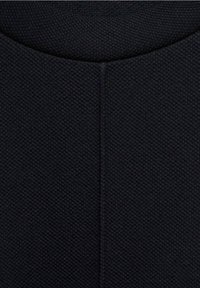 Tissu noir texturé avec un motif tissé, présentant une couture centrale et un col arrondi.