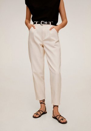 Frau trägt beige Hose mit hoher Taille und vorderen Taschen, schwarzen Gürtel, schwarzes ärmelloses Oberteil und schwarze flache Sandalen mit Riemchen.