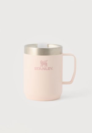 Taza de metal aislada de color rosa claro con asa y borde plateado, con el logo de Stanley que incluye un león alado y una corona.