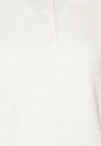 Detailní záběr na krémově zbarvenou pletenou tkaninu se dvěma malými knoflíky na texturované košili nebo svetru.