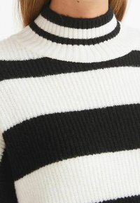 Gestreifter Pullover in Schwarz und Weiß mit hohem Kragen, gerippter Textur und auffälligen abwechselnden horizontalen Streifen. Weicher, gestrickter Stoff.