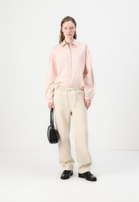 Light pink button-up shirt with oversized sleeves, beige cotton sweatpants with drawstring, black handbag, and black leather shoes.