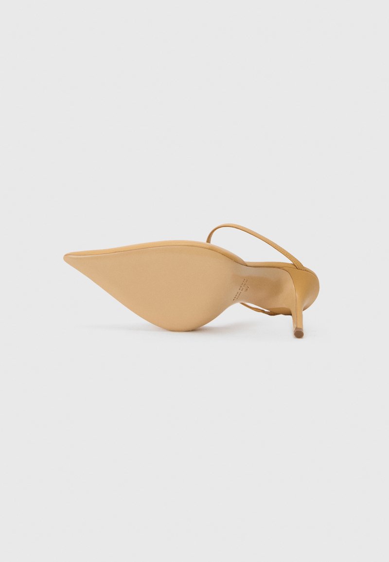 Sandale à talon haut beige à bout pointu avec une fine lanière autour de la cheville, présentée semelle vers le haut sur fond blanc.