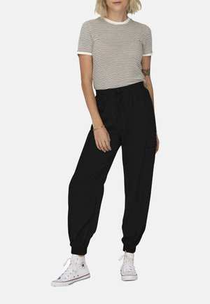 Joggers noirs avec ceinture élastique et chevilles resserrées, dotés de poches latérales, associés à un t-shirt ajusté à rayures. Des baskets blanches complètent l'ensemble.