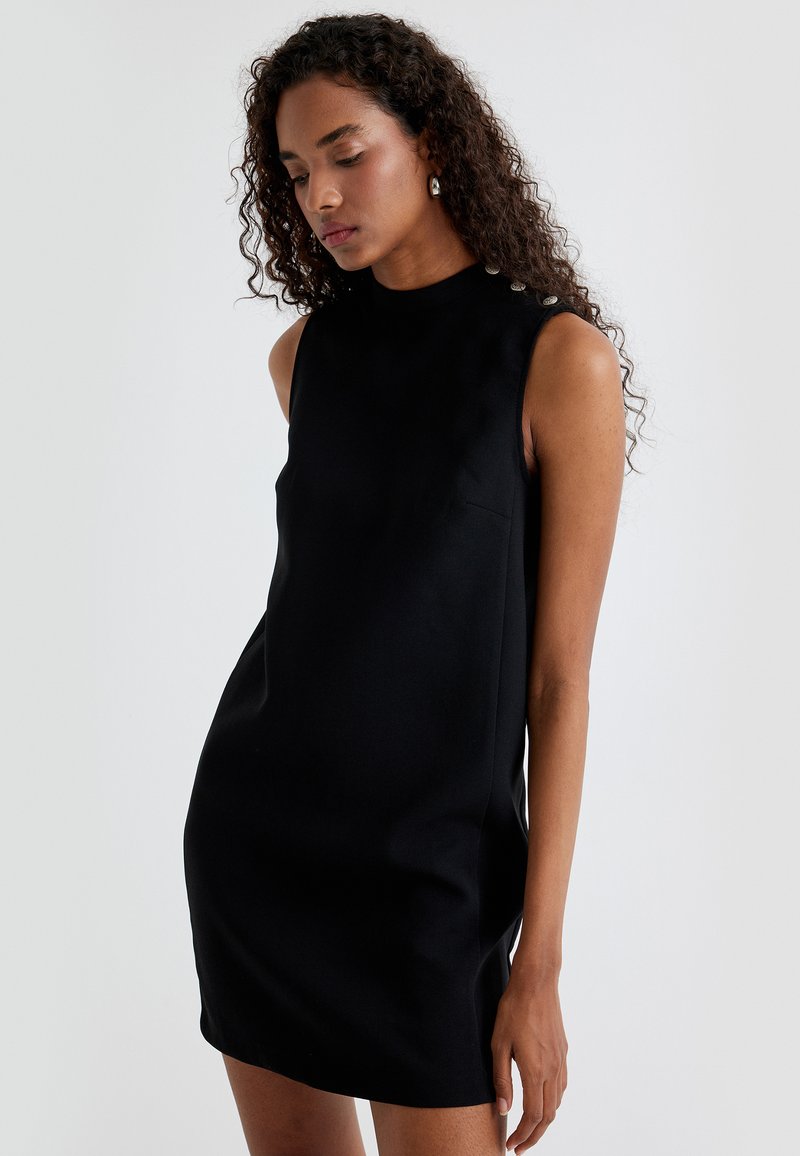 Schwarzes ärmelloses Kleid mit hohem Ausschnitt, minimalistischem Design, glattem Stoff und silbernen Knopfakzenten an den Schultern.