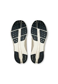 Scarpe atletiche con tomaia beige chiaro e suola in gomma nera. Le suole presentano un motivo testurizzato e ritagli esagonali per una migliore aderenza.