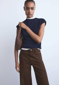 Marineblauw geribbelde top met korte mouwen, witte halstrim; bruin hoog-waisted broek; model met een bruine handtas; gladde stof, minimalistisch ontwerp.