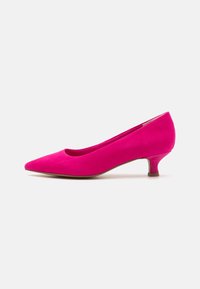 Escarpin en suède rose avec un bout pointu et un talon bas et fin. Sa texture douce et ses lignes épurées mettent en valeur sa silhouette élégante.
