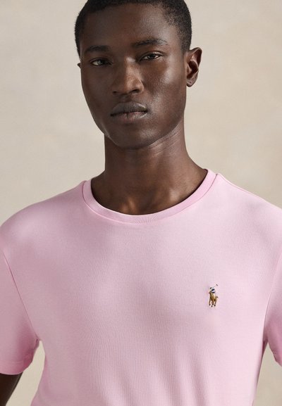 Rožinė medvilninė marškinėliai su apvalia iškirpte ir trumpomis rankovėmis. Kairėje krūtinės pusėje siuvinėtas mažas žirgo raitelio logotipas.