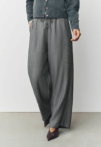 Gray wide-leg trousers with a textured finish, drawstring waist, and side pockets, paired with pointed, dark burgundy shoes.