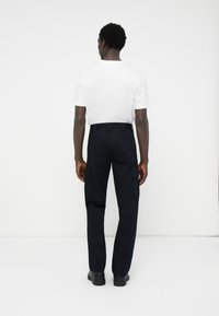 Calças de carga azul marinho com corte reto, múltiplos bolsos laterais e um cinto. Usadas com uma t-shirt branca simples e sapatos pretos.