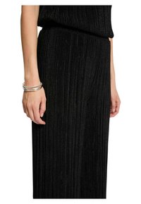 Pantalones de punto acanalado negros con rayas verticales, con una cintura alta. La muñeca del modelo muestra una pulsera plateada de varias bandas.