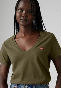 Camiseta de algodón verde olivo con escote en V, mangas cortas y un pequeño parche rojo de Levi's en la parte frontal. Corte casual.