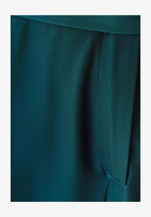 Donkerblauwgroene stof met een gladde textuur, met een zijnaad en subtiele stiksels, die doen denken aan een kledingontwerp.