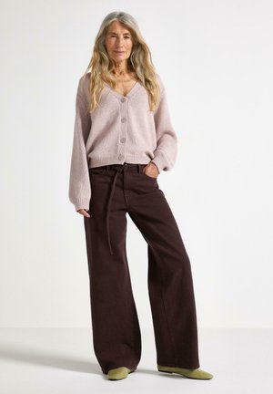 Ljusrosa cardigan med knappar, kombinerad med vida bruna byxor och gröna slip-on skor. Outfiten har en avslappnad passform och mjuk textur.