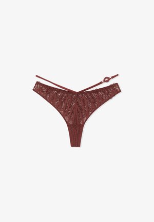 Lace bikini thong in deep burgundy, featuring a floral pattern, intricate cut-outs, and adjustable straps with a circular hardware accent.
