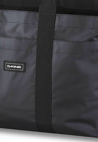 Borsa a tracolla nera realizzata in materiale durevole, con un design piatto a tinta unita e un'etichetta prominente con testo in grassetto. Include manici resistenti.