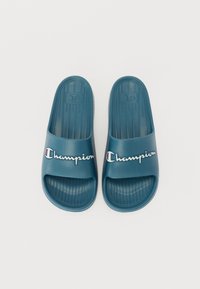 Infradito in gomma verde acqua con soletta testurizzata, cinturino largo con logo bianco "Champion" e accenti in rosso e blu.