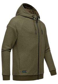 Hoodie vert olive en tissu texturé, avec une fermeture éclair à l'avant, une capuche réglable avec cordon et des poches latérales. Présente un patch logo sur l'ourlet.
