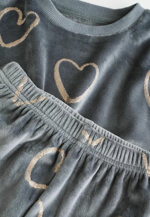 Grå velour loungewear sæt med en langærmet top med gyldne hjerteprint og matchende bukser med elastisk talje og lignende detaljer.