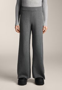 Široké tmavosivé nohavice vyrobené z mäkkej, textúrovanej látky s rebrovaným pásom, skombinované s robustnou čiernou obuvou.