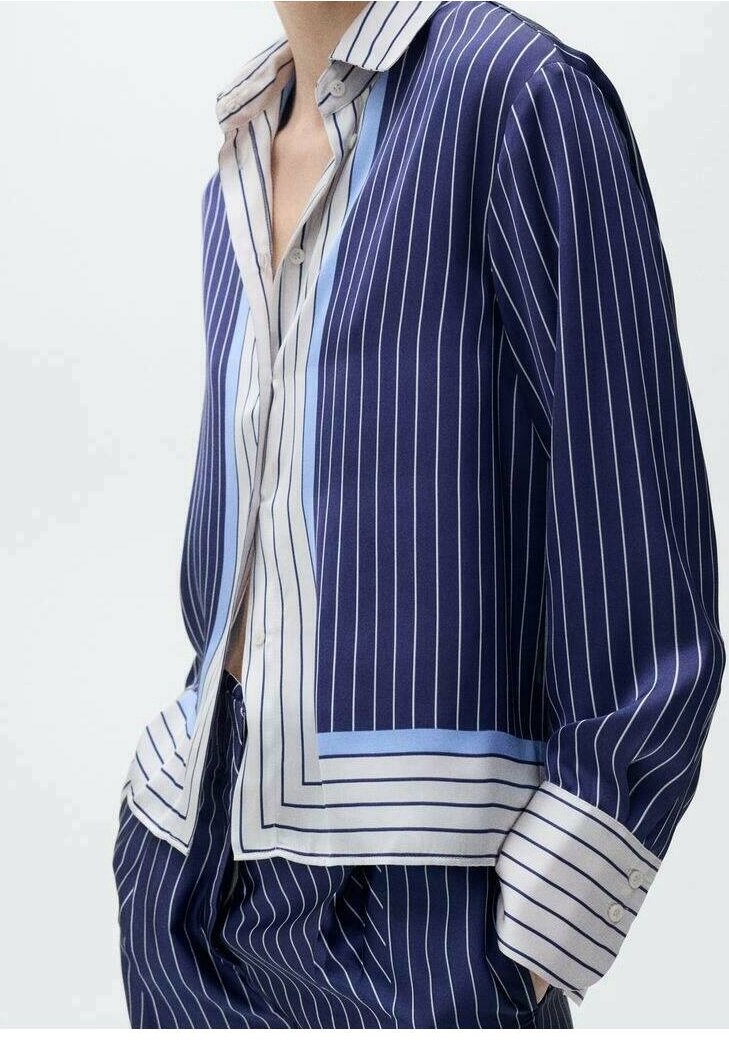 Personne portant une chemise rayée bleu marine et blanche et un pantalon assorti, les mains dans les poches et le col ouvert.