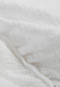 Weißer bestickter Stoff mit floralen Mustern und feiner Textur, der kleine Lochdetails und ein zartes, weiches Erscheinungsbild aufweist.