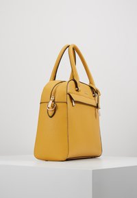 Żółta skórzana torebka o teksturowanym wykończeniu, o strukturalnym kształcie, z podwójnymi uchwytami, zamknięciem na zamek błyskawiczny oraz złotymi akcentami w hardware.