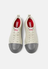 Sneakers con lacci in pelle color avorio con punta in gomma grigia, presentano una soletta rossa e il marchio 'CAMPER' sulla linguetta.