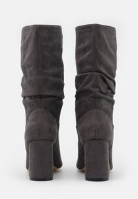 Bottes à talons hauts en daim gris avec un design décontracté, bout carré et talon bloc. Finition texturée avec de subtils détails de couture.