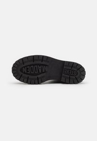 Semelle de chaussure en caoutchouc noir avec une surface texturée, présentant des crampons profonds pour une meilleure adhérence et le nom de marque en relief "STEVEN WADDEN."
