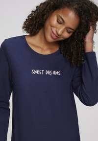 Navy long-sleeve top made of soft fabric, featuring a round neckline and the text "SWEET DREAMS" in light pink cursive embroidery.