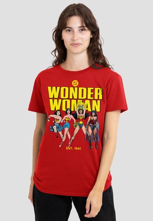 Young woman wearing a red Wonder Woman T-shirt featuring four different Wonder Woman illustrations and bold yellow text.
