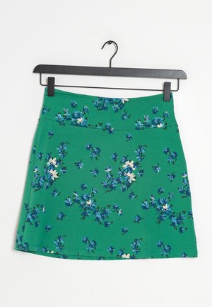 Groene rok met blauw-wit bloemmotief hangend aan een zwarte hanger tegen een witte achtergrond.