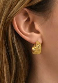 Boucle d'oreille en or avec un design en maille complexe et un accent floral. Forme courbée avec une finition lisse, portée dans une oreille.