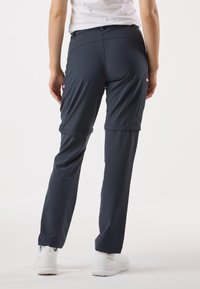 Granatowe spodnie outdoorowe o dopasowanym kroju, z elastycznym pasem i kieszeniami na zamek. Tkanina wydaje się lekka i trwała.