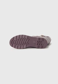 Semelle d'une botte en caoutchouc violet avec un motif texturé, présentant de profondes rainures et des crêtes pour l'adhérence, un talon plat et des éléments de design minimalistes.