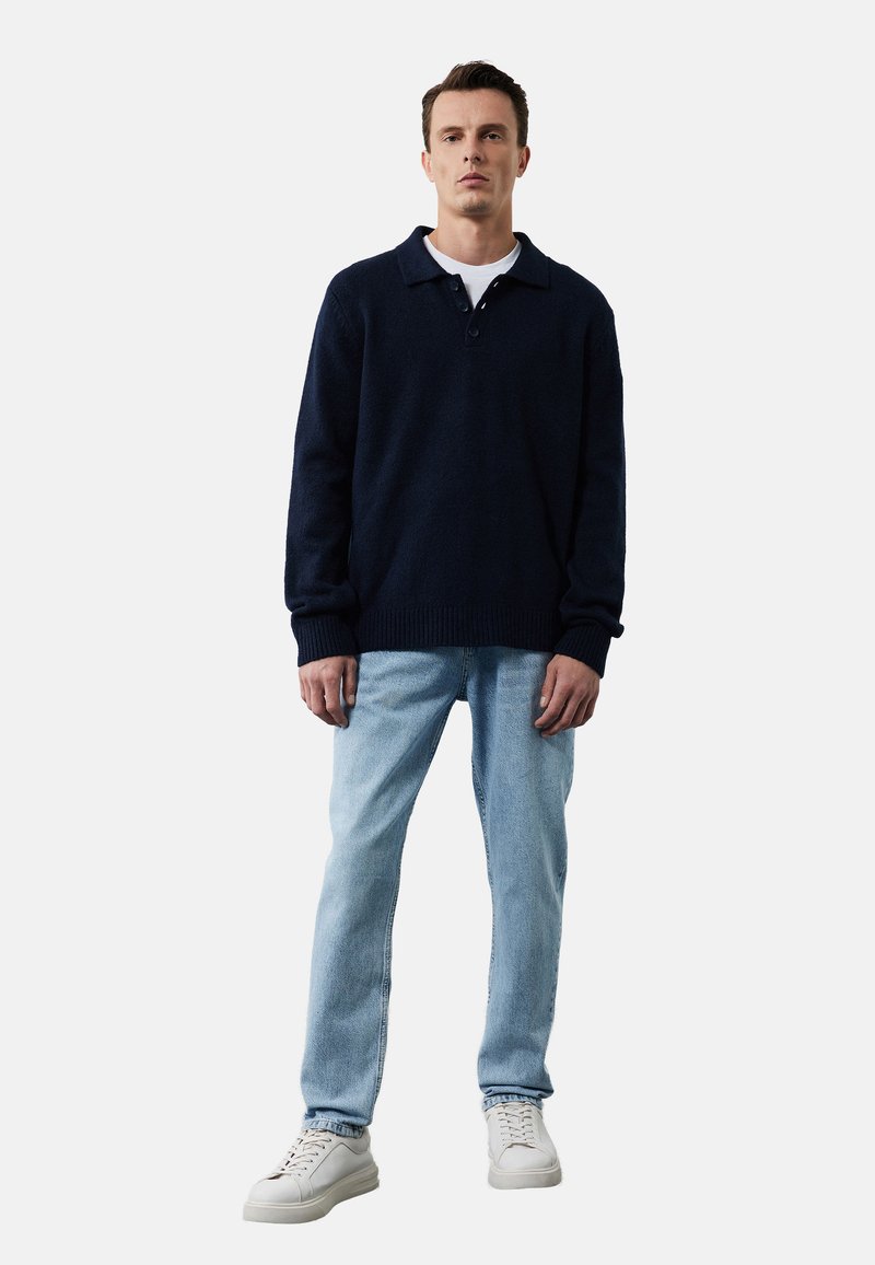 Granatowy sweter robiony na drutach z kołnierzykiem i dwoma guzikami, połączony z jasnoniebieskimi dżinsami i białymi trampkami. Luźny krój.