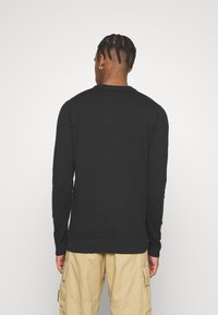Maglione nero a maglia, con collo rotondo e maniche lunghe, finitura a costine su polsini e orlo, mostrato da dietro, abbinato a pantaloni cargo color khaki.