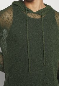 Hoodie verde a maglia con finitura testurizzata, dotato di cappuccio con cordino e maniche in pizzo trasparente per un aspetto stratificato.