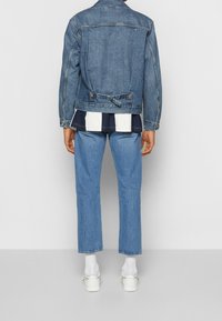 Denimjacka i medelblått med en ryggknutdetalj, bärs över en marinblå och vit randig skjorta samt ljusblå jeans, ihop med vita skor.