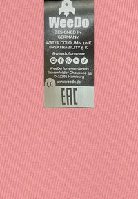 Roze stof met verticale ribbelstructuur en een grijze waslabel met tekst, sociale media icoontjes en bedrijfsinformatie.