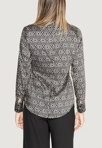 Blusa a maniche lunghe a fantasia bianca e nera, con orlo arrotondato e dettagli a taglio sui polsini. Tessuto morbido e tessurizzato.