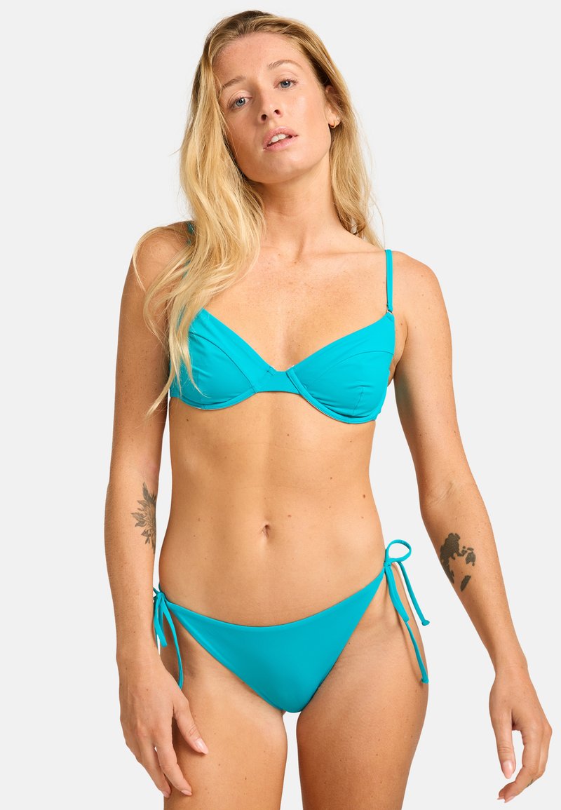 Completo bikini turchese con top a coppe triangolari e spalline regolabili, e slip laterale con lacci, realizzato in tessuto liscio con dettagli minimi.