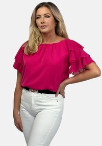 Fuksjowa bluzka z falbaniastymi rękawami, luźny fason, miękka faktura, okrągły dekolt, połączona z białymi dżinsami i czarnym paskiem.