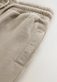 Beige Sweatpants mit Kordelzugbund, weichem Material, seitlichen Taschen und einfachen Nähdetails. Der Stoff wirkt leicht und glatt.