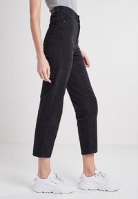 Jeans negros de tiro alto, hechos de denim, con corte recto, con un desgaste mínimo y diseño de cinco bolsillos. Combinados con zapatillas blancas.